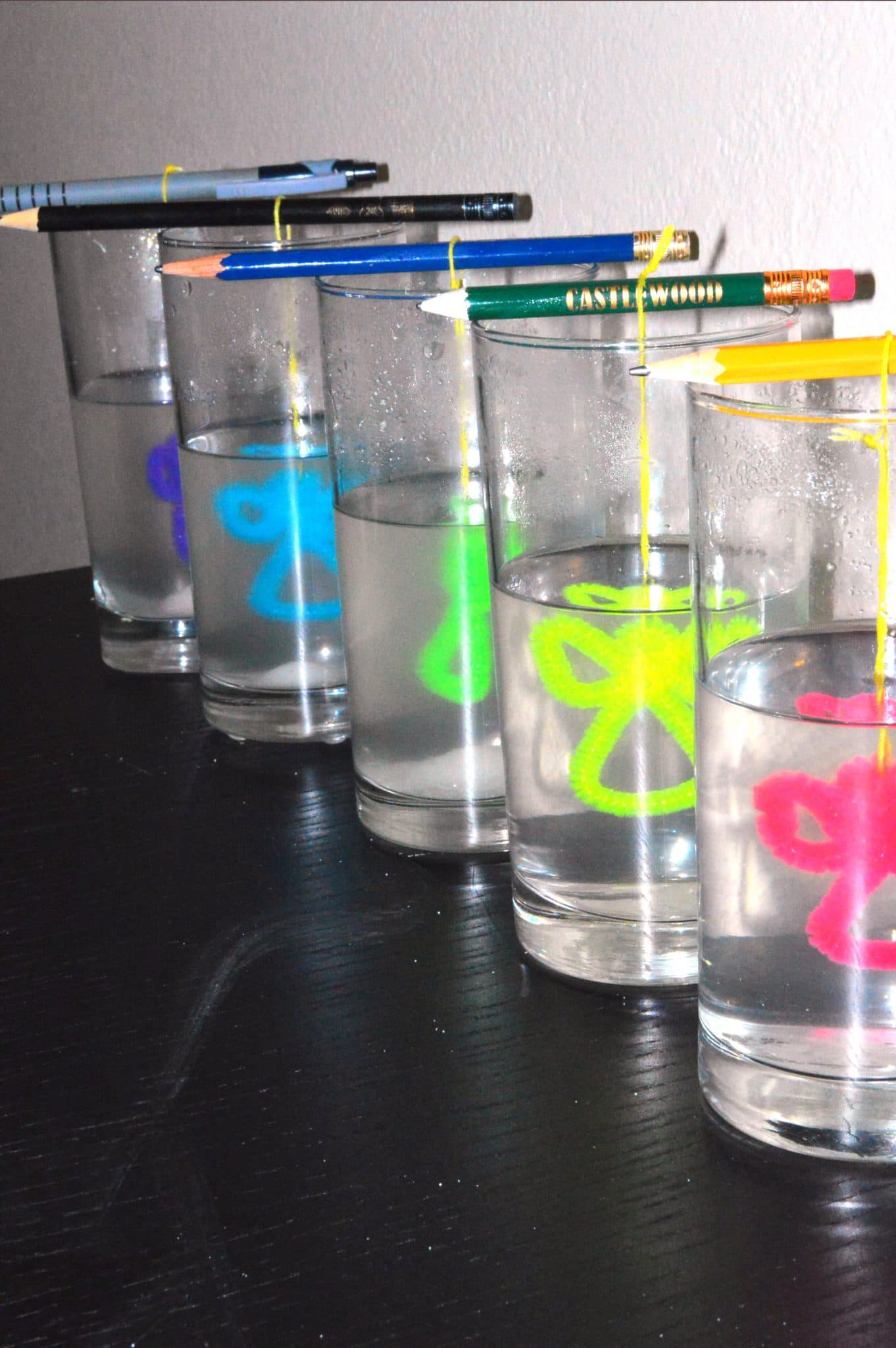 angel pipe cleaners are dangled from pencils into glasses with water