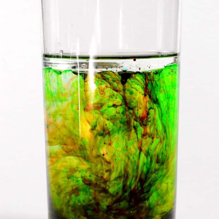 a glass of water with different color mixing together in traces