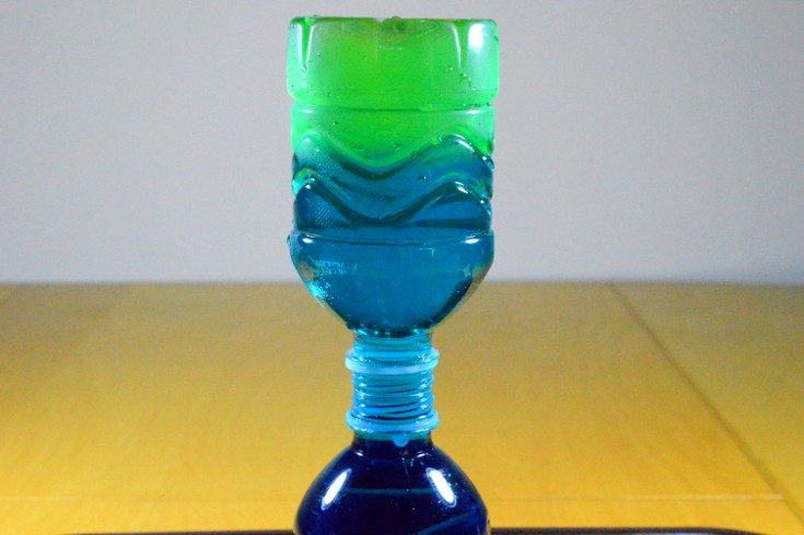 bottle of green-blue water is placed upside down on top of a bottle of dark blue water