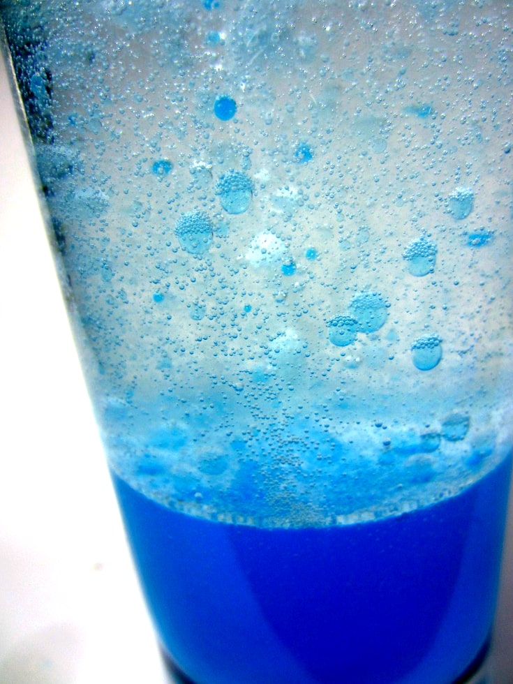 Blue water and baby oil inside a clear glass, with blue bubble rising, makes a Lava lamp using baby oil.