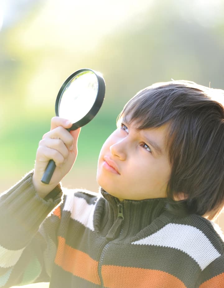 Boy looks into magnifying glass to investigate, Scientific method example.