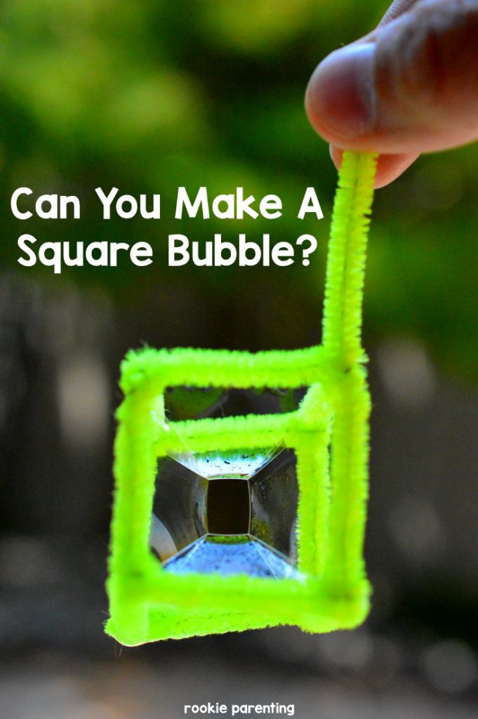 Hand holds a green pipe-cleaner that contains a square cube bubble.