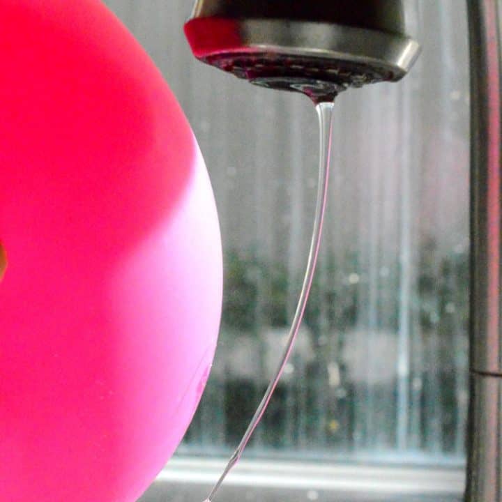 water stream from facet bends towards a pink balloon